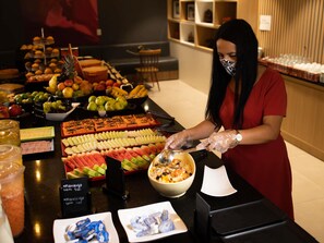 Disposição de buffet com diversos alimentos e uma pessoa servindo.