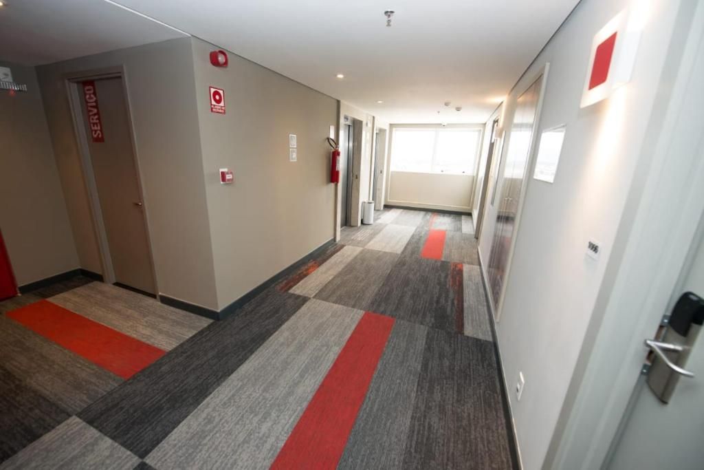 Corredor de hotel com carpete xadrez, um extintor e uma porta com a inscrição 'SERVICIO'.