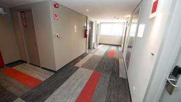 Corredor de hotel com carpete xadrez, um extintor e uma porta com a inscrição 'SERVICIO'.