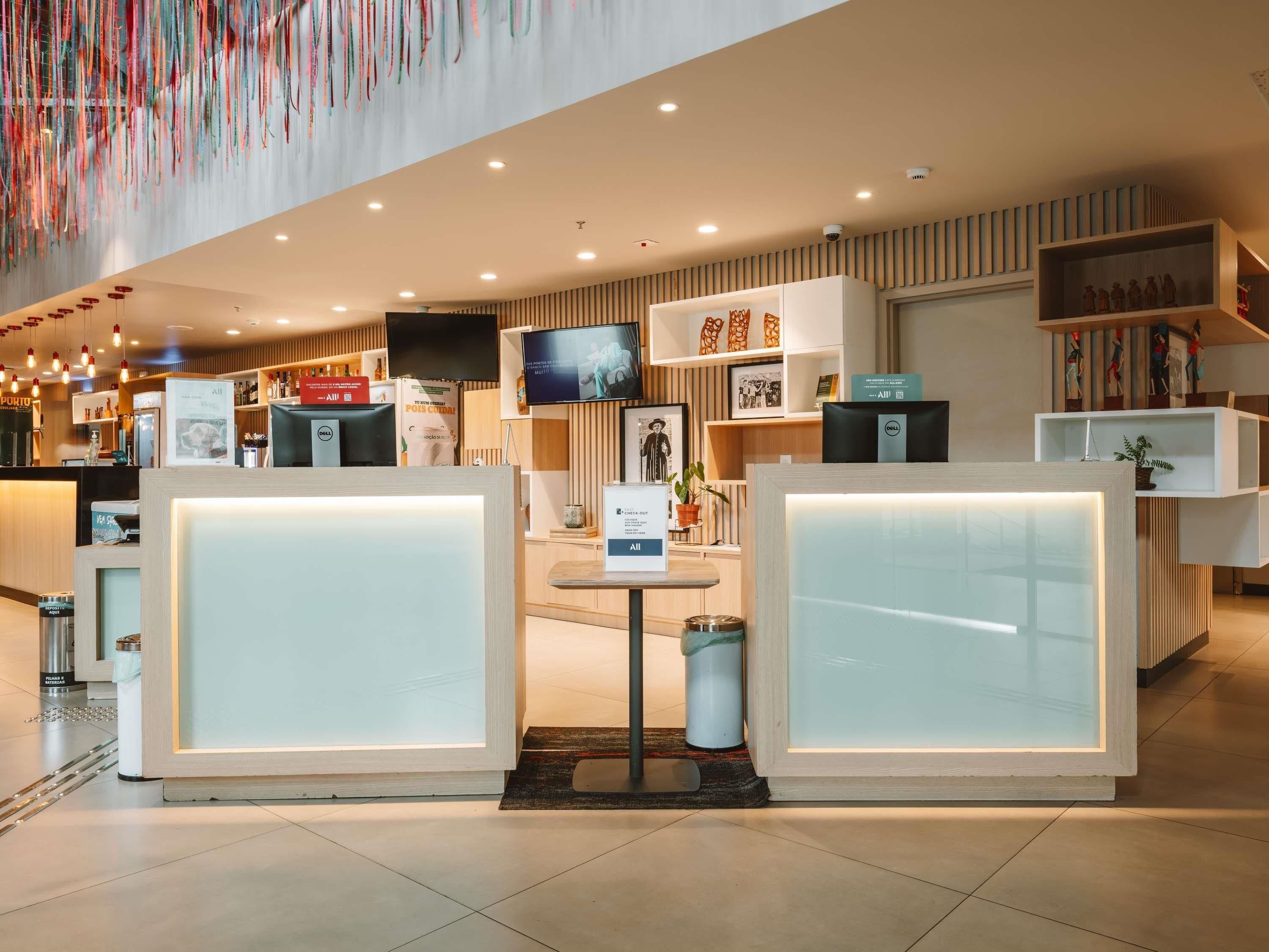 Una hall d'albergo moderna con reception, televisore e diversi servizi.