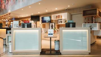 Una hall d'albergo moderna con reception, televisore e diversi servizi.