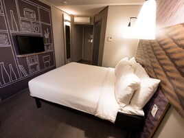 Quarto de hotel com cama, televisão na parede, ar condicionado e luminária.