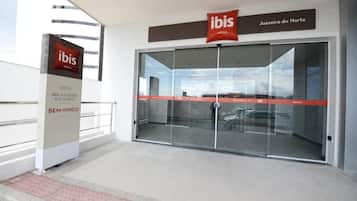 A hotel entrance with glass doors, a sign for 'ibis Hotels Juazeiro do Norte', and a 'BEM-VINDO' sign.