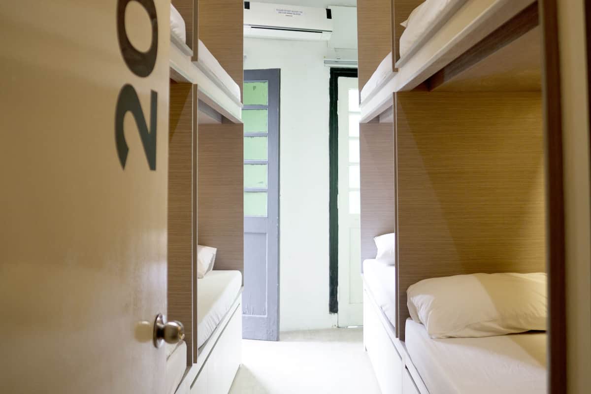 A narrow hallway with two beds, each with white bedding and a wooden headboard.