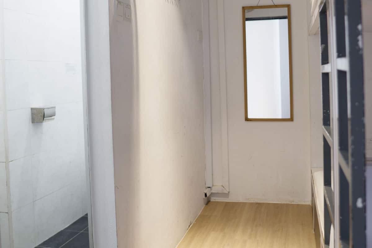 A narrow hallway with white walls, a wooden floor, and a mirror on the right.