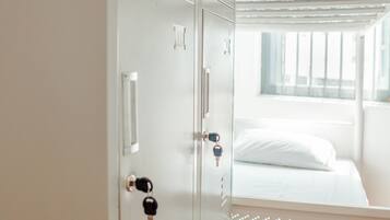 Una habitación de hotel con cama, ventana y armario metálico con llaves colgadas en la puerta.
