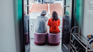 Two people sitting on ottomans at a balcony with a view of buildings and a rack of shoes. - BEAT. Sports Hostel (Singapore)
