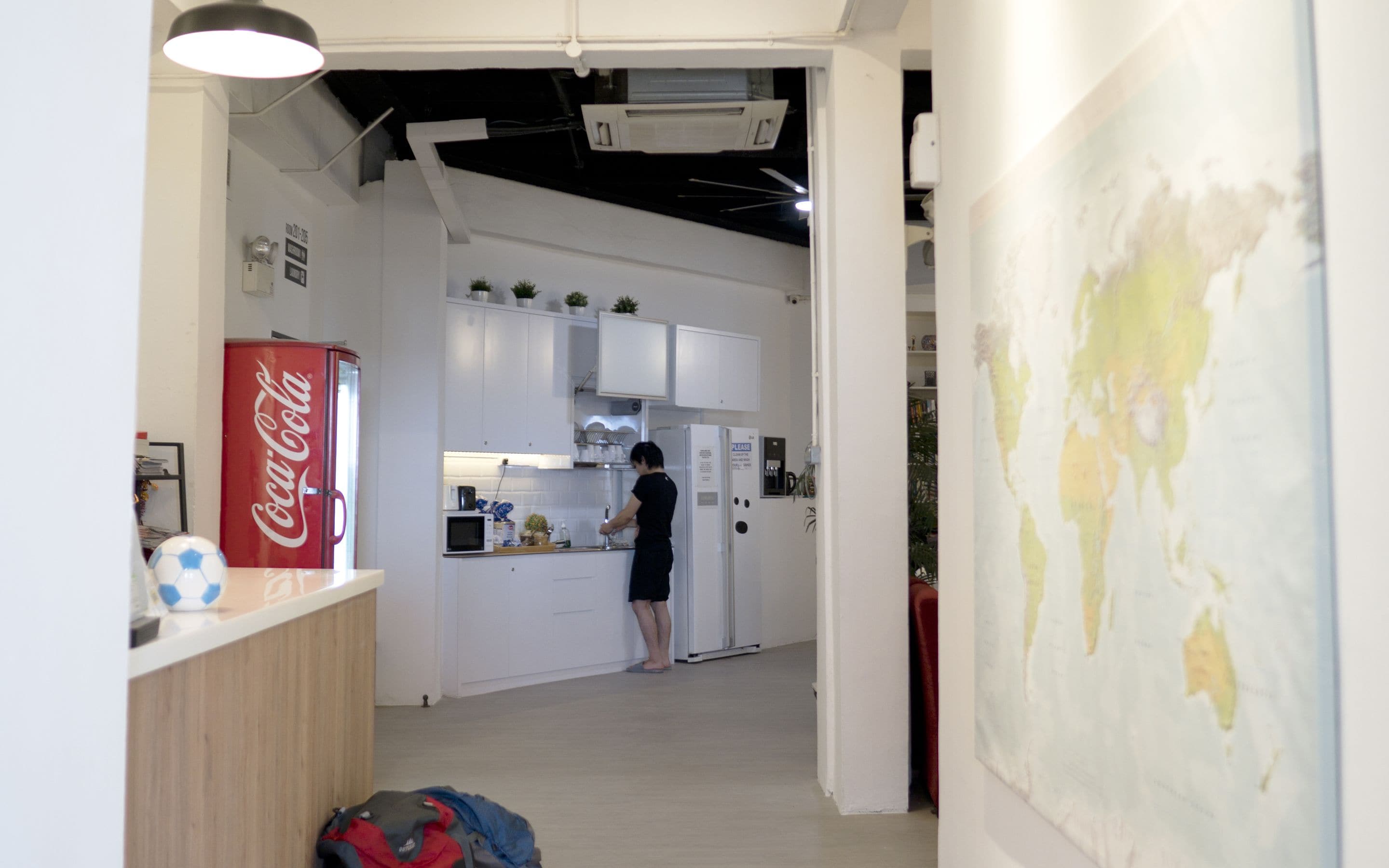 Eine moderne Küche mit weißen Schränken, einer Mikrowelle und einem Kühlschrank. Ein Coca-Cola Kühlschrank und eine Karte hängen an der Wand.