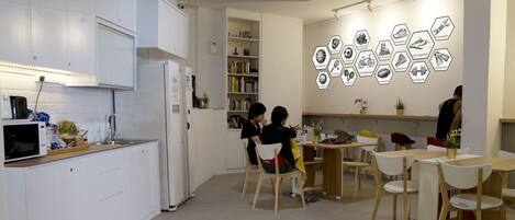 Una cocina moderna con armarios blancos, microondas integrado y un refrigerador. Hay sillas de madera y una mesa con un jarrón de flores.