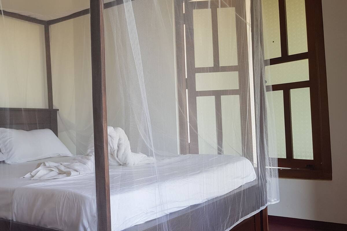 A four-poster bed with white linens and a mosquito net.
