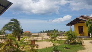 A beachside property with a yellow building, palm trees, and a sandy area. - Exotic Beach Hotel (Pottuvil)
