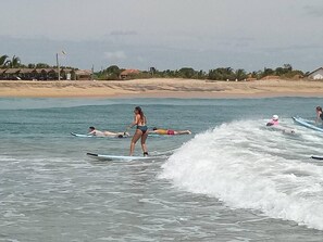 A beach with people on surfboards, a sandy shore, and buildings in the background. - Exotic Beach Hotel (Pottuvil)