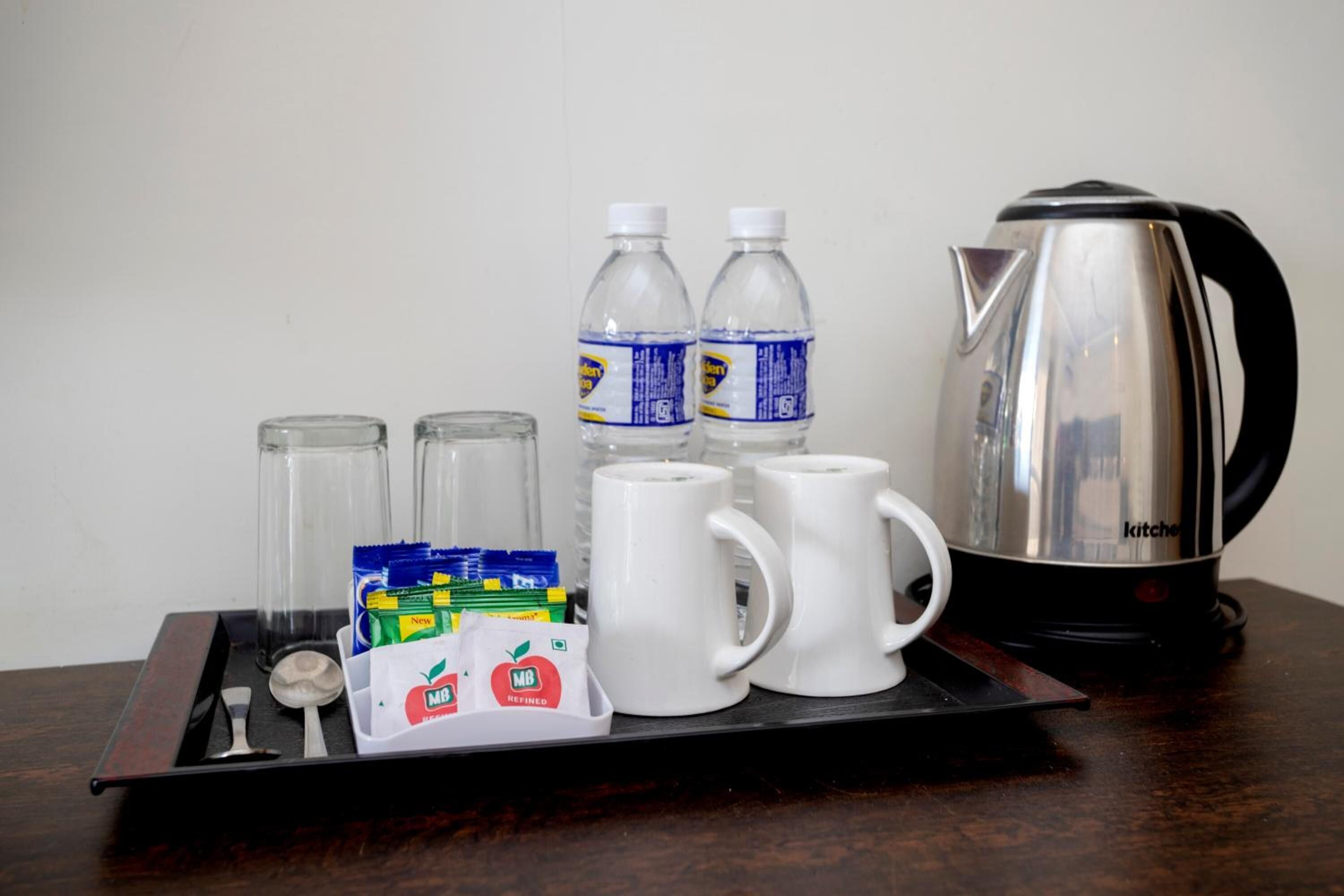 A tray with a kettle, two water bottles, two white mugs, a spoon, and a packet of tea bags.