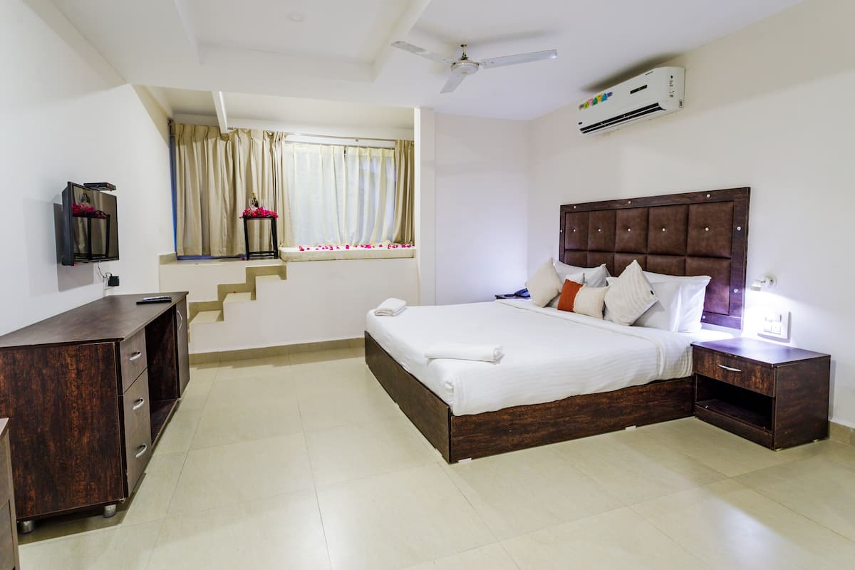 Habitación de hotel con cama, mesita de noche, televisor y ventana con cortinas.
