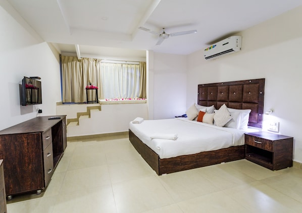 Habitación de hotel con cama, mesita de noche, televisor y ventana con cortinas.