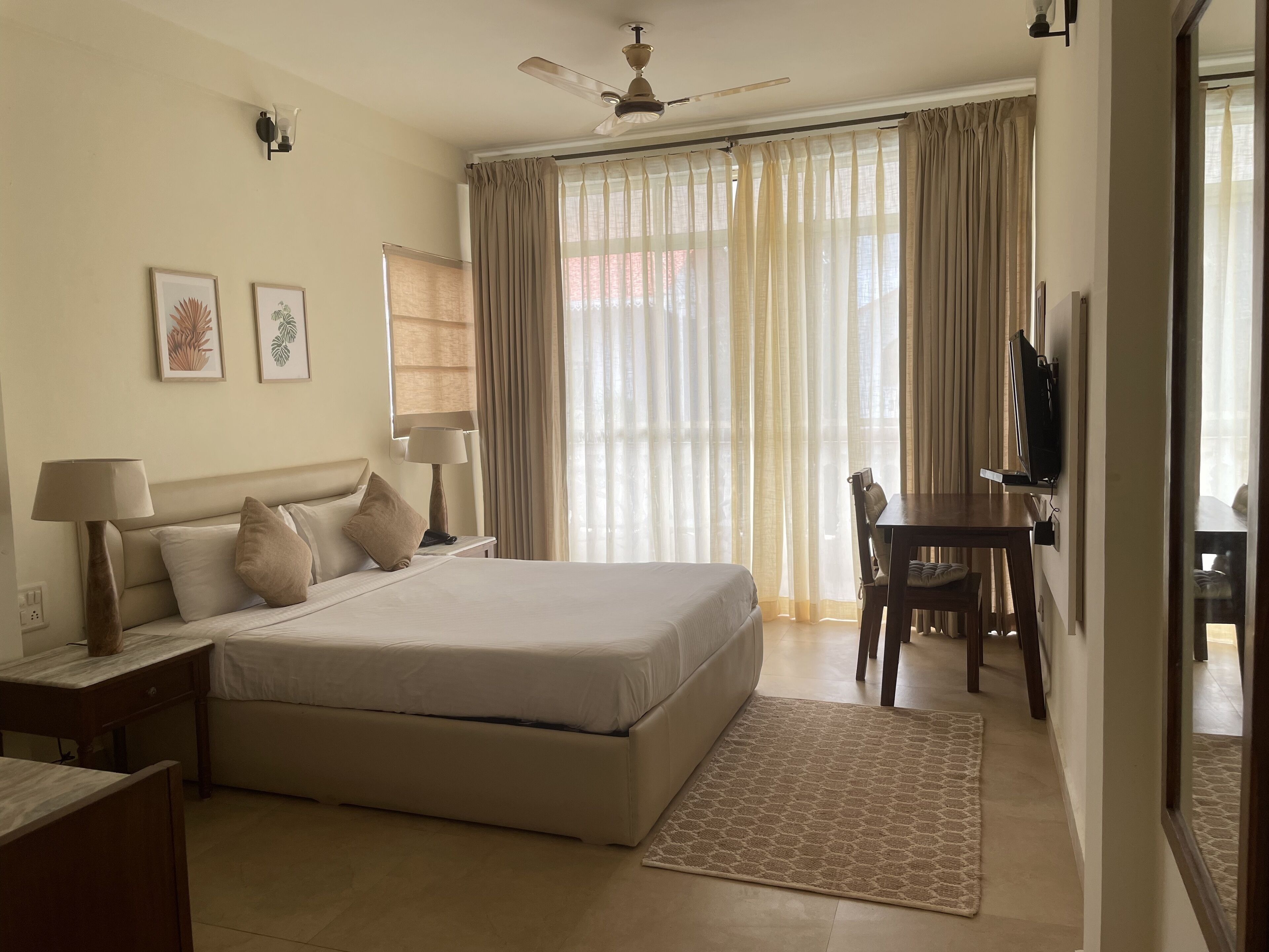 A hotel room with a bed, bedside tables, a desk, a chair, a TV, and a ceiling fan.