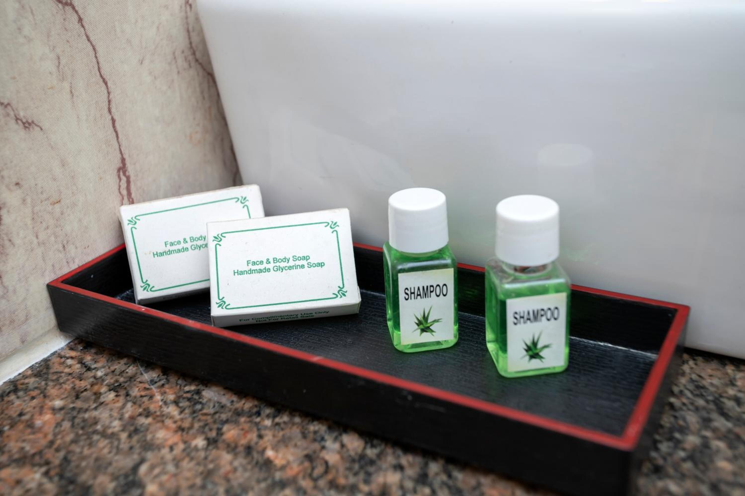 Un vassoio con due bottiglie di shampoo verde e due confezioni di sapone per viso e corpo su un piano di lavoro in granito.