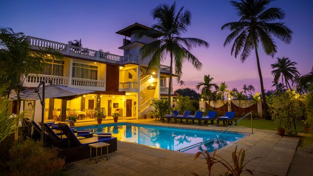 A two-story building with a swimming pool, lounge chairs, and palm trees. - La Vaiencia Beach Resort (Morjim)