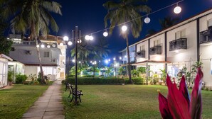 A well-lit courtyard with a pathway, palm trees, and a bench. - La Vaiencia Beach Resort (Morjim)