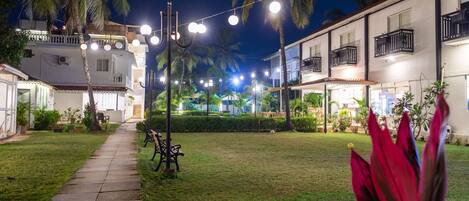 A well-lit courtyard with a pathway, palm trees, and a bench.