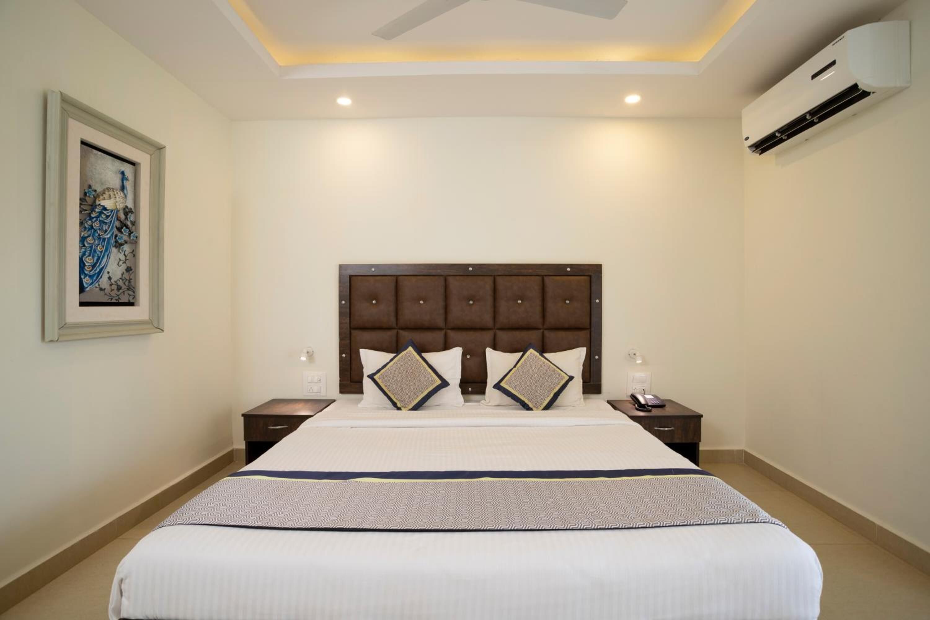 Habitación de hotel con una cama grande, cabecera, dos mesitas de noche y un equipo de aire acondicionado.