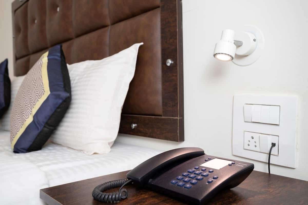 Habitación de hotel con cabecera de madera, teléfono en la mesita de noche, lámpara de pared y toma de corriente.