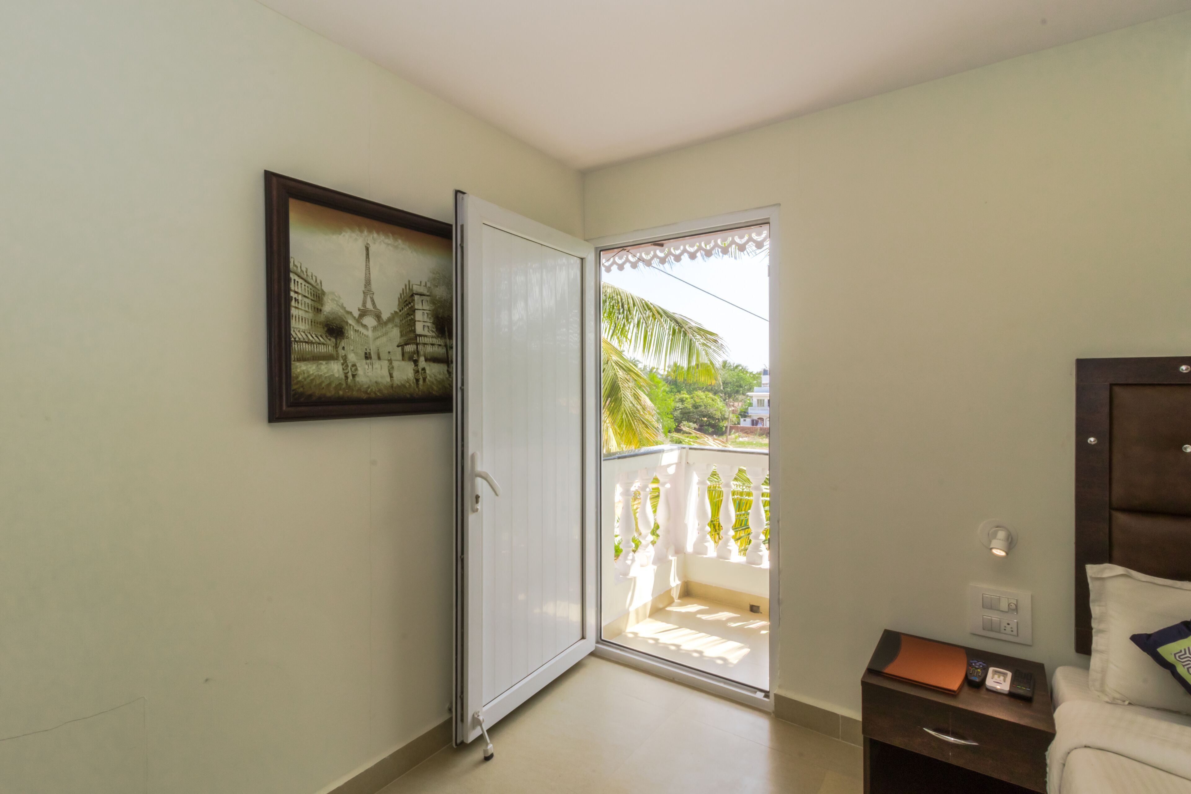 A bedroom with a bed, a nightstand, a framed picture, and a sliding glass door leading to a balcony.