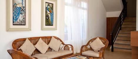 A living room with a sofa, two armchairs, a coffee table, and two framed peacock paintings on the wall.