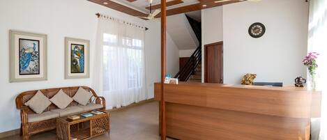 A reception area with a wooden reception desk, a sofa, and a coffee table. There are ceiling fans, a clock, and framed artwork on the walls.