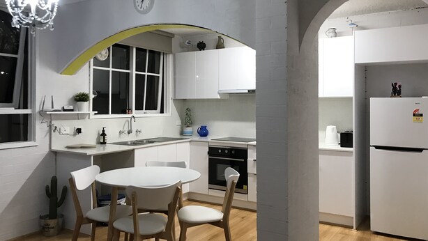 A modern kitchen with white cabinetry, a dining table with chairs, a chandelier, and a clock on the wall. - Santa Monica apartment (Carnegie)