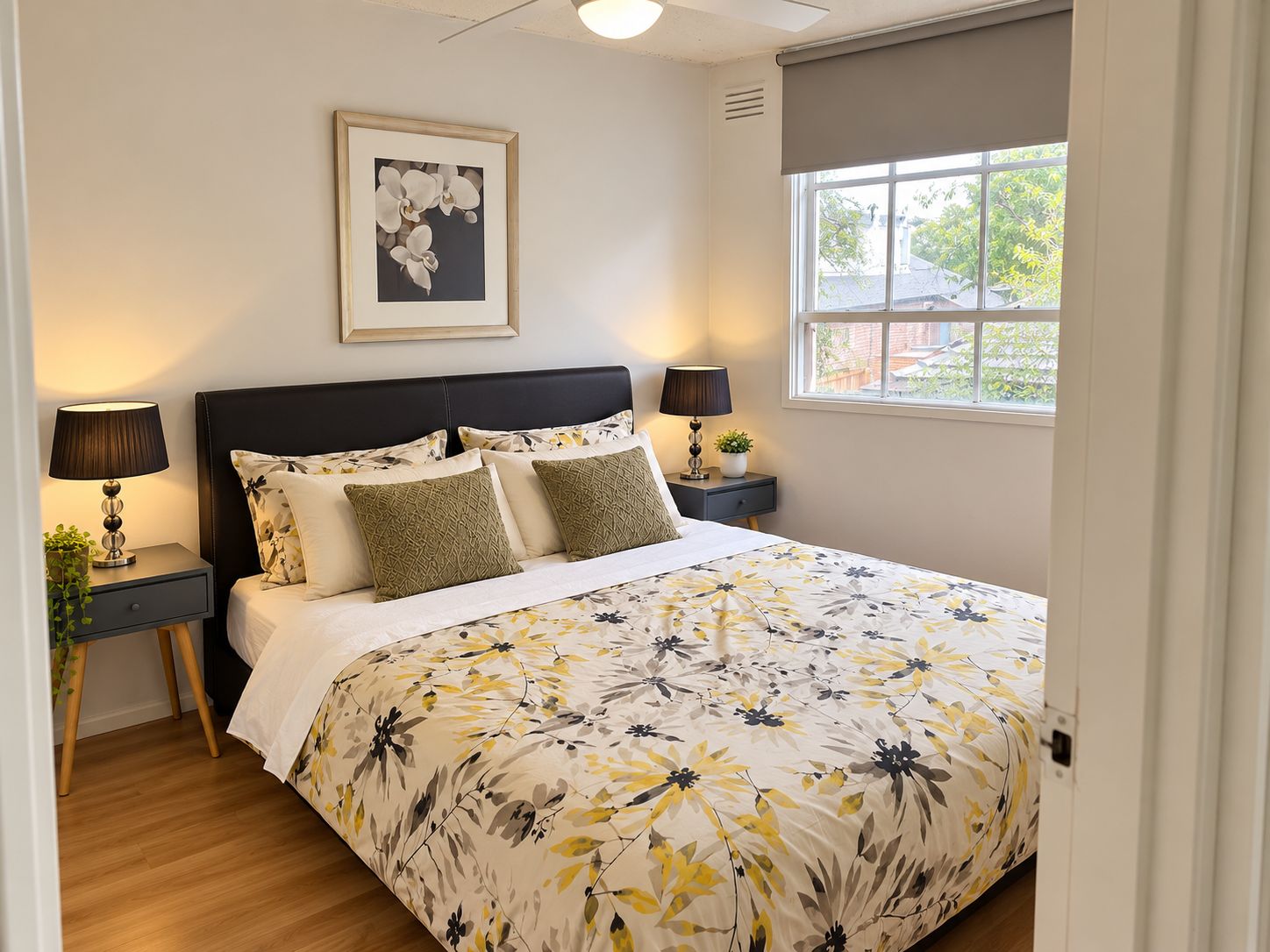 A bedroom with a bed, two bedside tables, a window, and a framed picture on the wall.