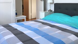A bedroom with a bed, a nightstand, a lamp, a ceiling fan, and a door leading to another room. - Santa Monica apartment (Carnegie)
