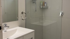 A modern bathroom with a glass shower enclosure, a white sink, and a mirror. - Santa Monica apartment (Carnegie)