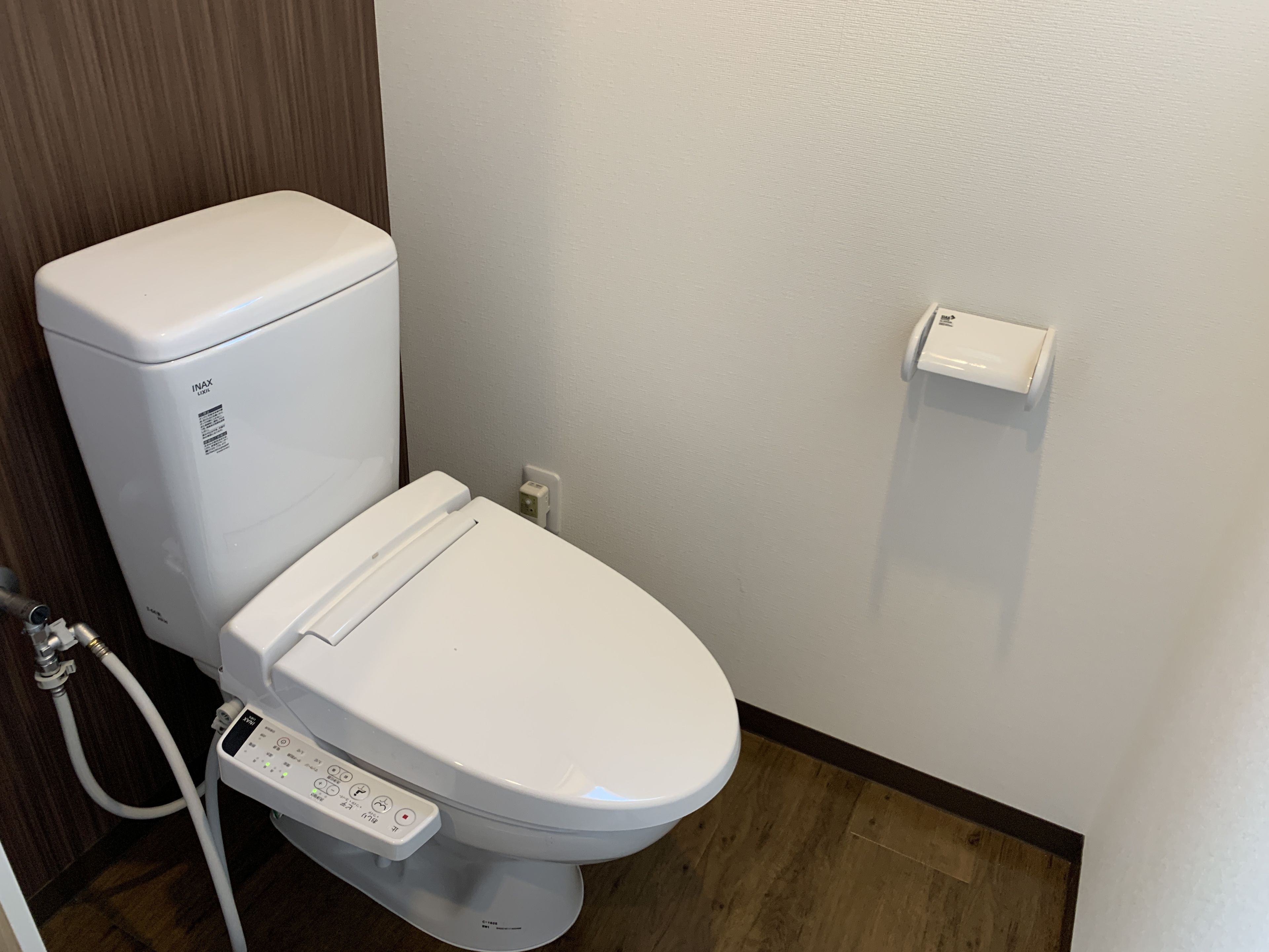 A modern bathroom with a white toilet, a control panel, and a wall-mounted bidet.