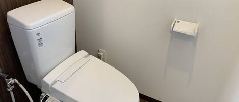 A modern bathroom with a white toilet, a control panel, and a wall-mounted bidet.