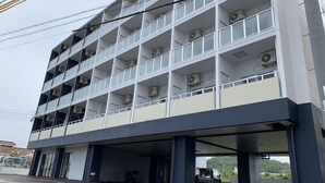 Un immeuble à plusieurs étages, doté de climatiseurs sur chaque niveau, d’un parking couvert et offrant une vue sur la verdure en arrière-plan.