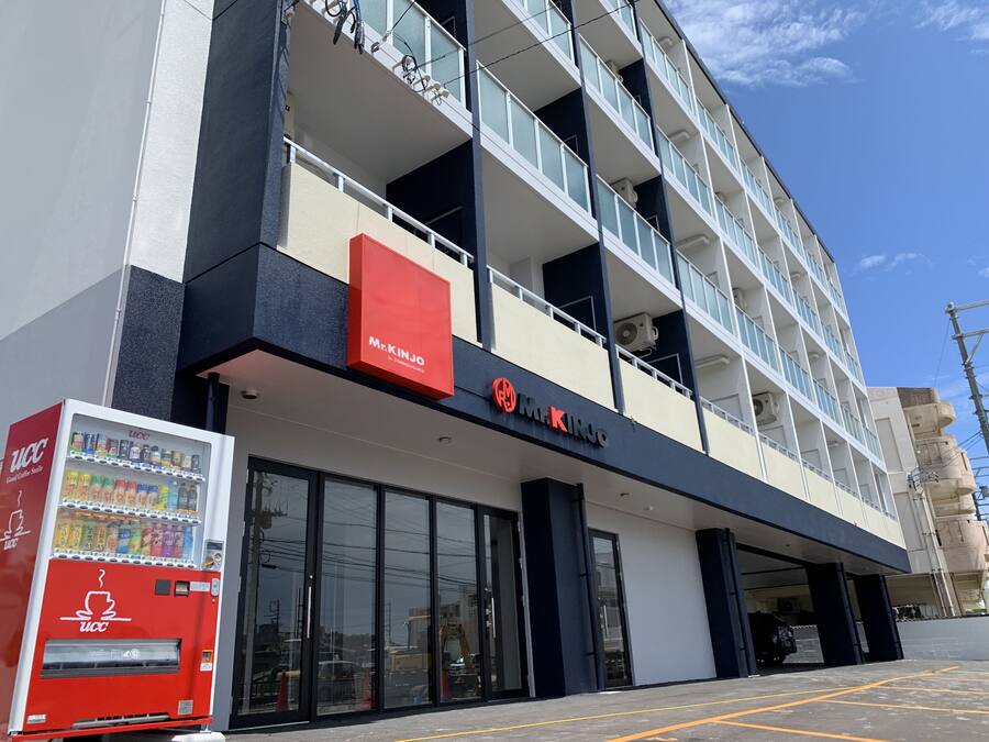 A multi-story building with a Mr. Kinjo store on the ground floor, a vending machine, and a parking area.