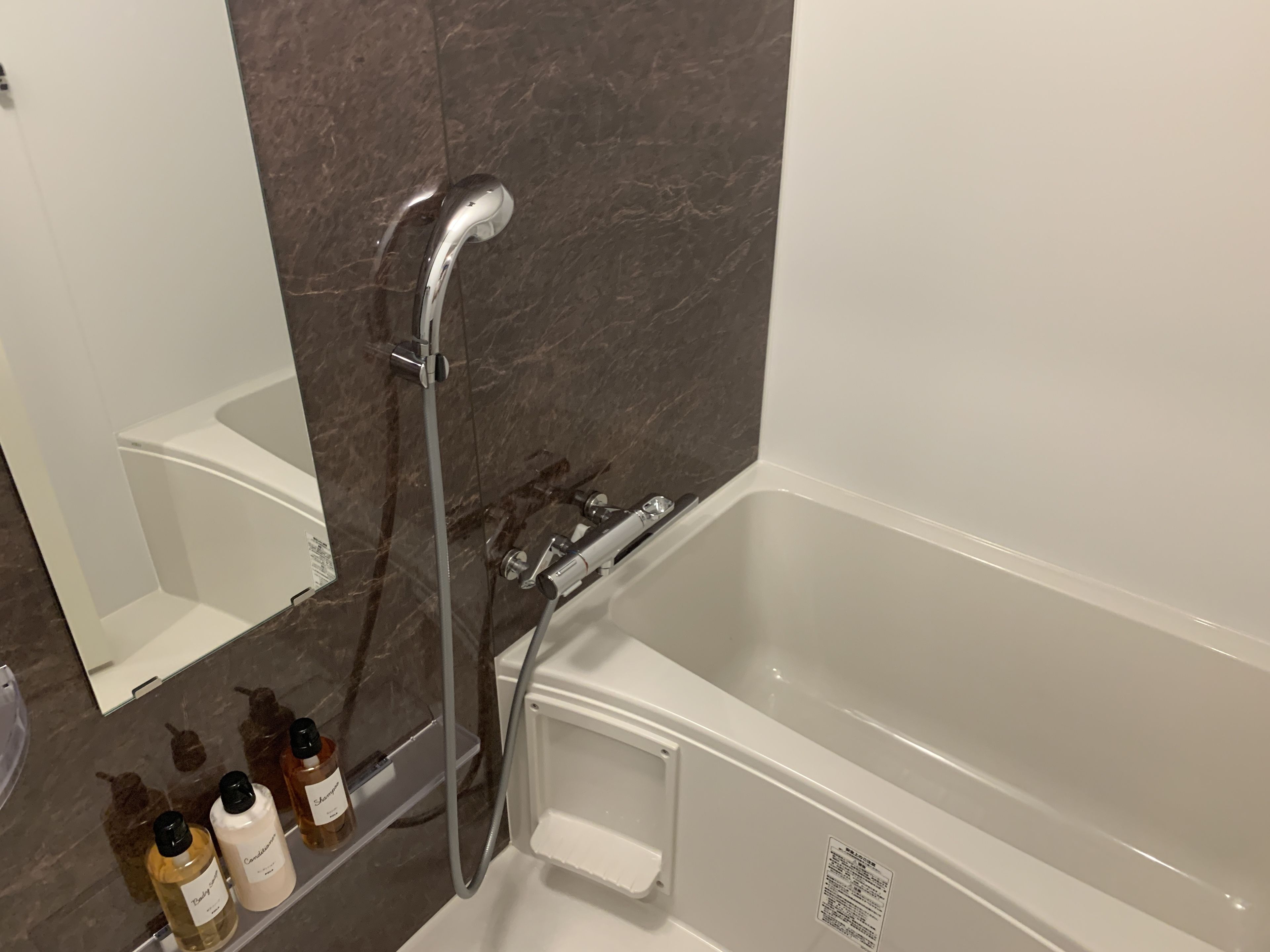 Une salle de bain moderne avec une baignoire, un espace douche et une étagère sur laquelle sont posées trois bouteilles de shampoing.