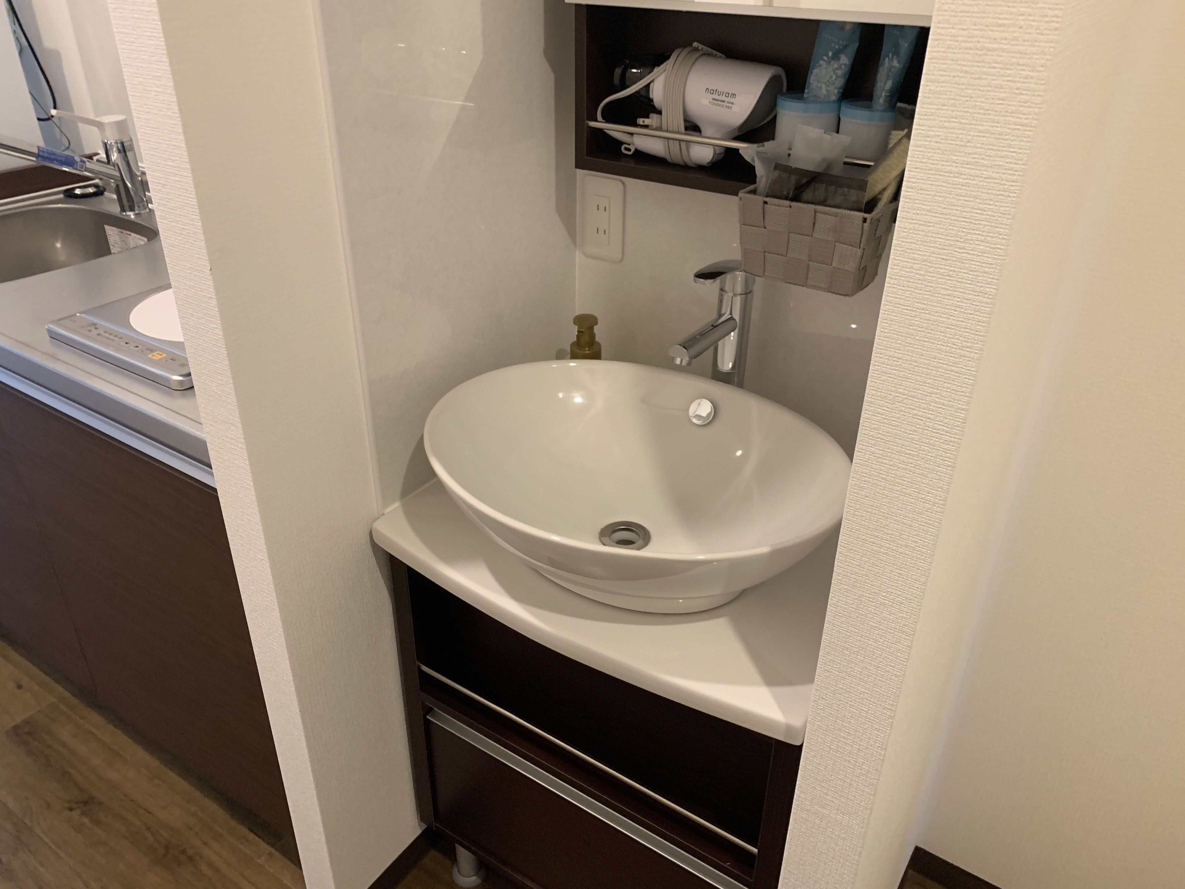 A bathroom with a white sink, a mirror, and a shelf with toiletries.