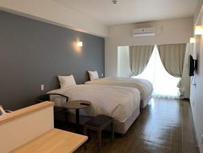 A hotel room with two beds, a small table, a bench, and a TV mounted on the wall. - Mr.KINJO in Tomigusuku (Tomigusuku)