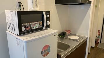 Een kleine keuken met een magnetron bovenop een koelkast, een spoelbak en een kookplaat.
