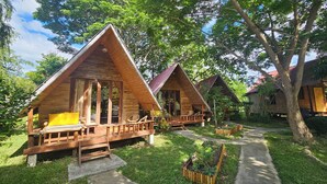A row of wooden triangular cabins with wooden decks and chairs, surrounded by lush greenery and trees. - Luxury Farm House (Pai)