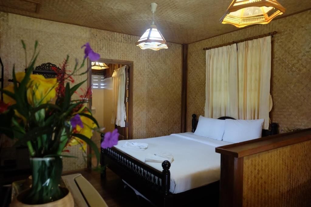 A hotel room with a bed, a nightstand, a vase with flowers, and a hanging light fixture.