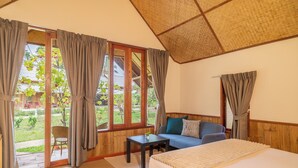 A bedroom with a bed, a sofa, a small table, and a view of a garden through large windows. - Luxury Farm House (Pai)