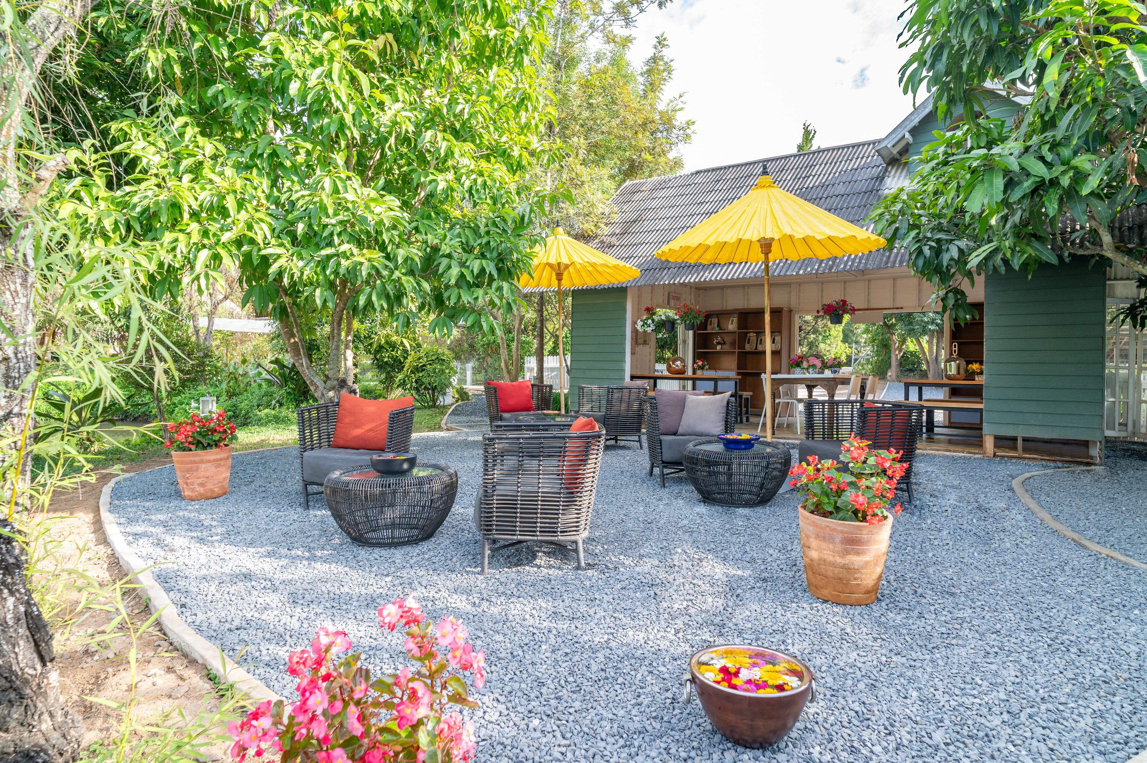 An outdoor seating area with wicker furniture and yellow umbrellas, surrounded by greenery and potted plants.