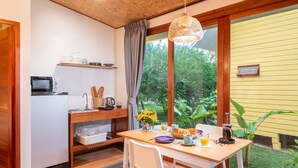 A kitchen with a wooden table, white chairs, a microwave, and a window with a view of greenery. - Luxury Farm House (Pai)