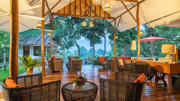 An outdoor covered patio area with wicker furniture, a wooden table, and a red umbrella. - Luxury Farm House (Pai)