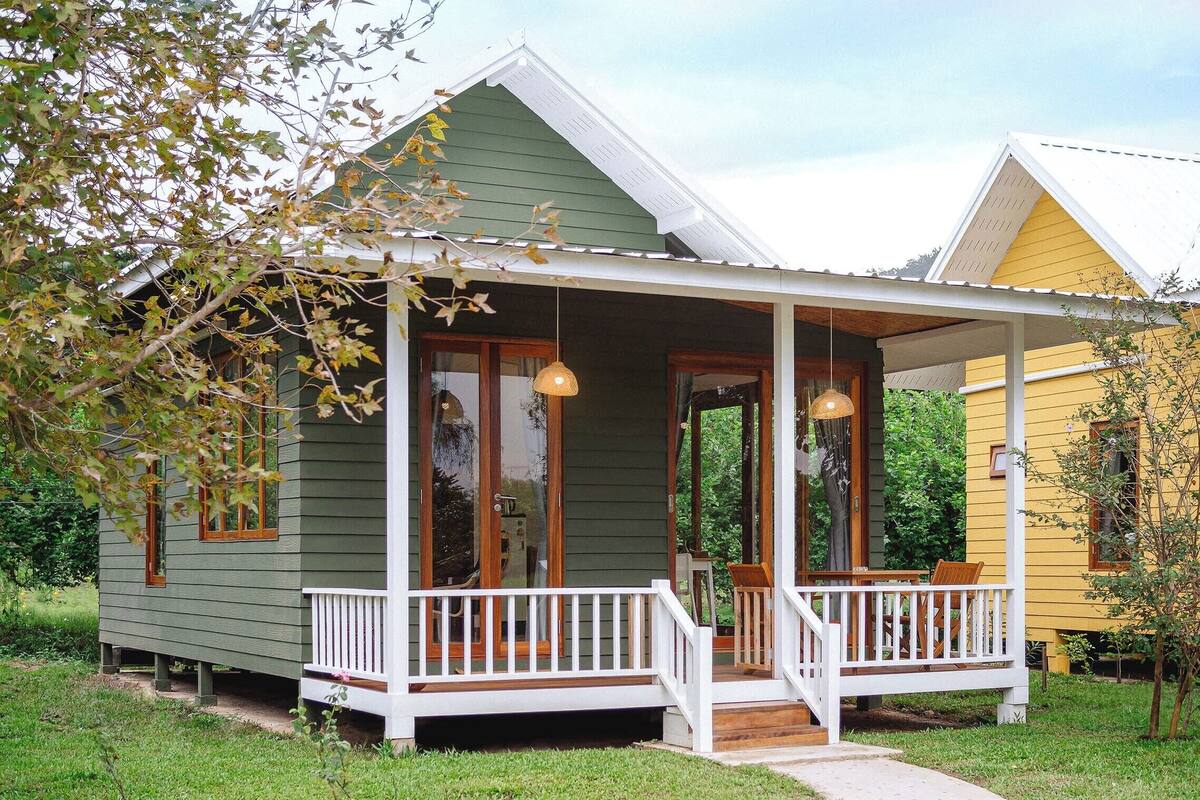 A green house with a porch and a yellow house in the background.