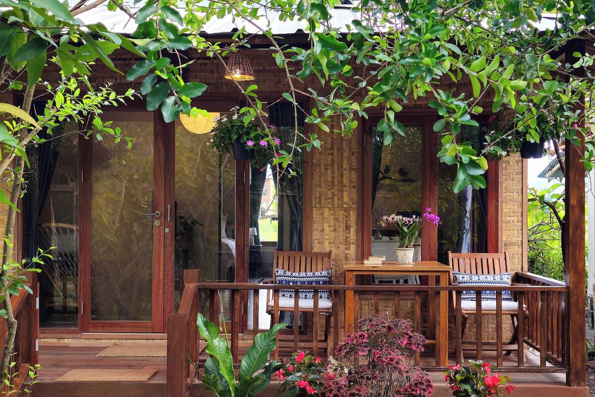 A wooden porch with a table and chairs, surrounded by potted plants and flowers.