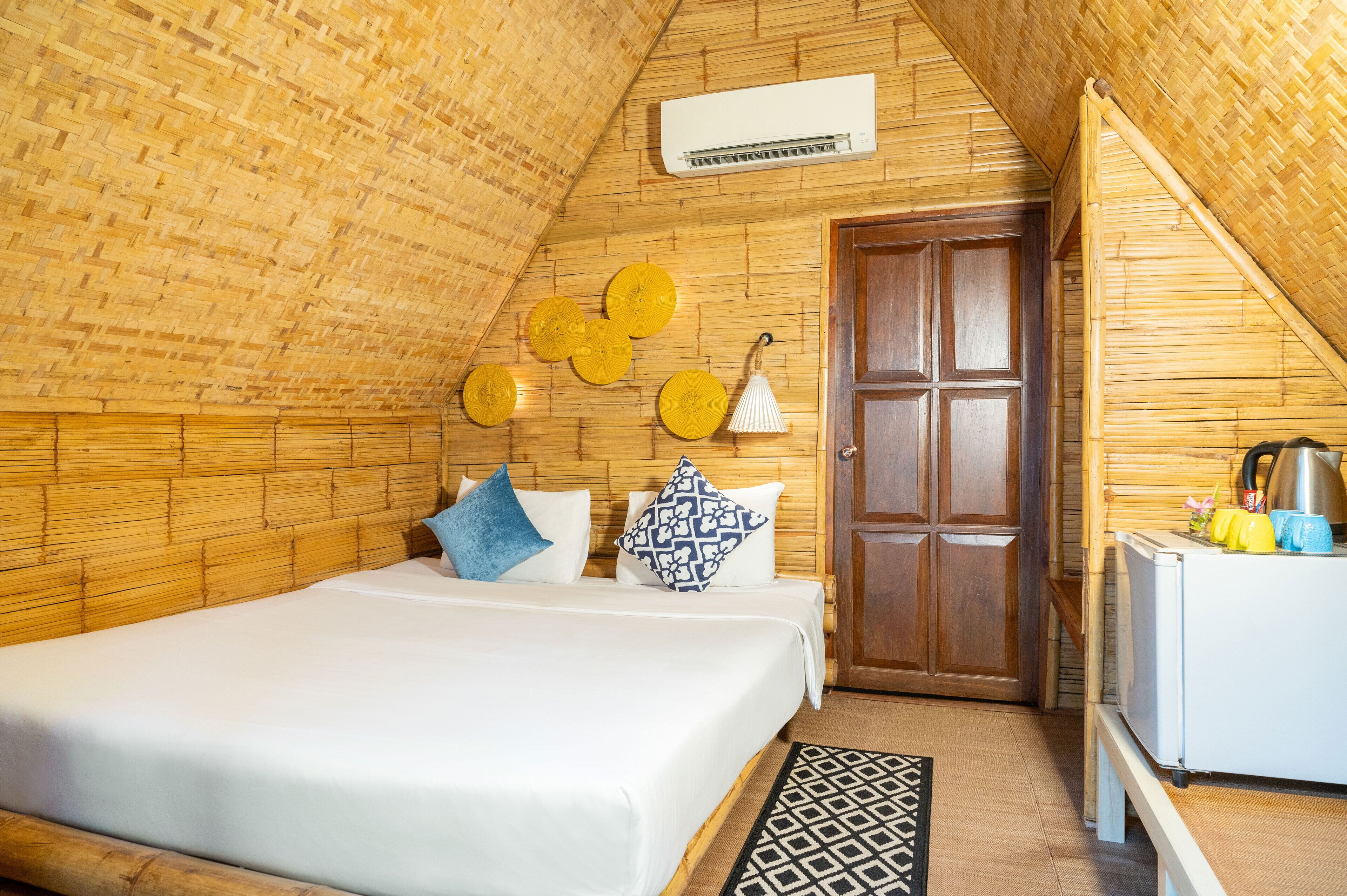 A cozy room with a bed, wooden walls, a door, and a small kitchenette.
